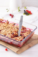 Apple and berry crumble, topped with oats in glass baking dish on white table. Crispy fruit pie, healthy summer dessert. Close-up.