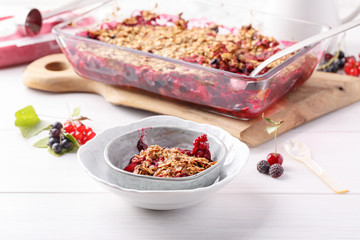 Apple and berry crumble, topped with oats in glass baking dish on white table. Crispy fruit pie,...