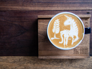 Cup of coffee with beautiful unicorn and tree shape latte art foam on wooden background with copy space. Top view.