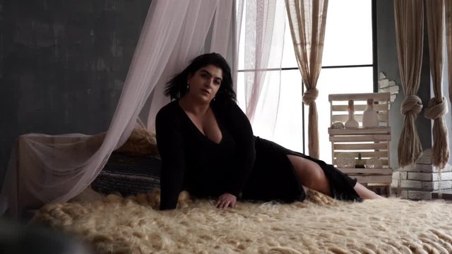 Model plus size with big cheeks and black hair lies almost naked on the bed
