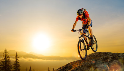Cyclist in Red Riding the Bike Down the Rock at Sunrise. Extreme Sport and Enduro Biking Concept. - obrazy, fototapety, plakaty