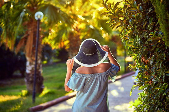 Young beautiful woman in beach hat walking under tropical palm trees at sunny day in Bodrum, Turkey. Vacation Outdoors Seascape Summer Travel Concept