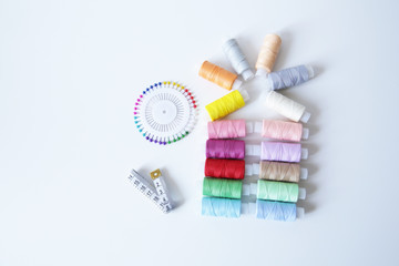 spools of colorful thread, meter and needles on white background. Flat lay. Top view. With copy space for text.