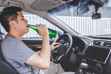 Young asian man drives a car with drunk a bottle of beer behind the wheel of a car