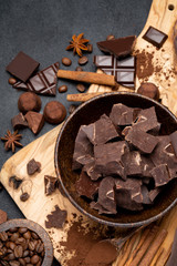 Dark or milk organic chocolate pieces and truffle candies in wooden bowl on dark concrete backgound