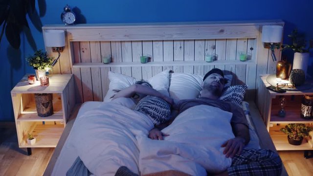 Snoring man. Couple in bed, man snoring and woman cannot sleep, covering ears with pillow for snore noise. Young interracial couple, Caucasian woman, Caucasian man sleeping in bed at home.