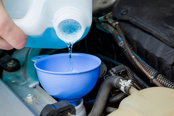 Man hands filling blue washer fluid in car tank through funnel from plastic bottle for windshield in garage. Care about automobile. Closeup. Front view.