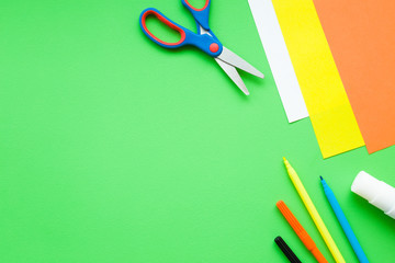 Naklejka premium Colorful application paper, scissors, glue stick and color pens on green desk for kids. Hobby of children. Empty place for text, quote or sayings.