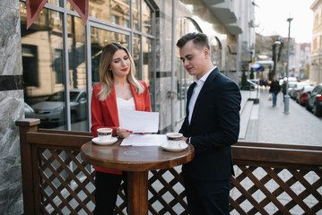 Two confident business colleagues walking on office terrace. Mid adult business man and woman discussing document outdoors on coffee break. Working during break concept