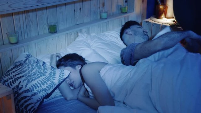 Young man annoyed by the snoring of his female partner sleeping in bed at night, covers his head with a pillow. A man unable to sleep because of the snoring sound. Health issues, conflict trouble