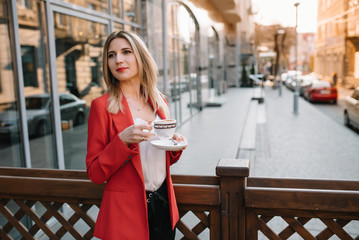 Beautiful young businesswoman with a disposable coffee cup, drinking coffee, and holding tablet in her hands against urban city background.