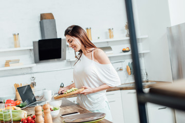 Cheerful girl holding chopping board with cut bananas and avocados