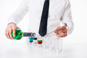 Fototapeta premium Bartender pours alcoholic drink into small glasses on bar. Colorful cocktails at the bar.
