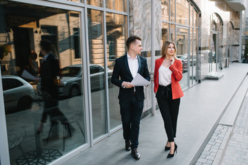 Obraz premium Two confident business colleagues walking on office terrace. Mid adult business man and woman discussing document outdoors on coffee break. Working during break concept