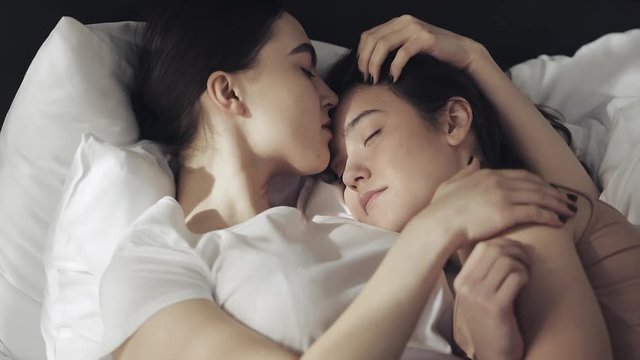Lesbian couple embracing in the bed at home. One girl kisses another girl when she is sleeping Slow motion. Lifestyle, LGBT concept