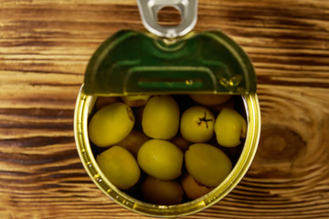 Open tin can of green olives on wooden table. Top view