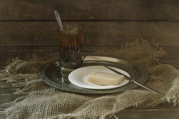 A piece of cheese on a plate and a glass of tea.