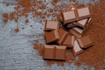 Dark or milk organic chocolate pieces and cocoa powder on dark concrete backgound