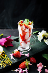Glass with icecream and slice od strawberry, leavs of mint decorated on table with flowers and fruits