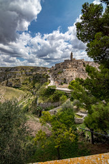 Fototapeta na wymiar Summer day scenery street view of the amazing ancient town of the Sassi with white puffy clouds moving on the Italian blue sky. Matera, Basilicata, Italy