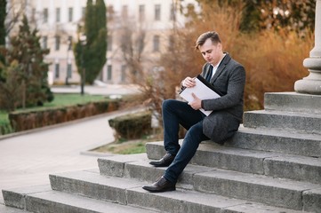 Obraz premium Handsome young businessman working with documents sitting on the stairs outdoor
