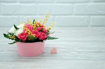 Creative bouquet of flowers with a pink heart against the background of a white loft, on a wooden table. Spring bright bouquet in a pink decorative bucket.