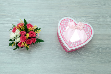 A creative bouquet of flowers with a box in the shape of a heart lies on a wooden table. Gift beloved girlfriend.