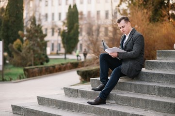 Obraz premium Handsome young businessman working with documents sitting on the stairs outdoor