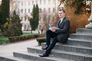 Obraz premium Handsome young businessman working with documents sitting on the stairs outdoor