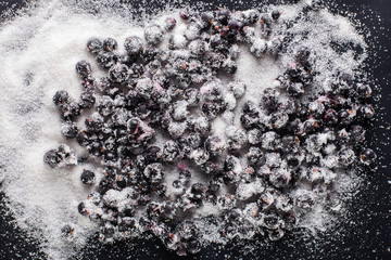 Photo of frozen black currants with sugar on a black background with water