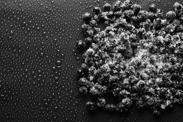 Photo of frozen black currants with sugar on a black background with water