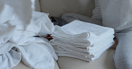 Woman folding clean soft towels on sofa at home