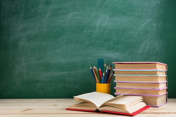 Education and reading concept - group of colorful books on the wooden table in the classroom, blackboard background