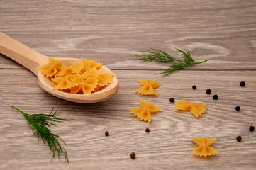 Bow-shaped pasta in a large wooden spoon with allspice on a gray wooden table.