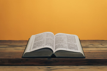 Fototapeta na wymiar Open Holy Bible on a old oak wooden table. Orange wall background..