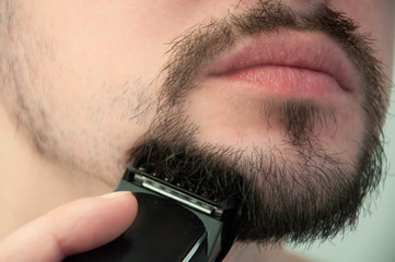 A young guy shaves in the bathroom. The guy shaves his beard with a trimer. Care beard.