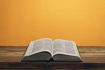 Fototapeta na wymiar Open Holy Bible on a old oak wooden table. Orange wall background..
