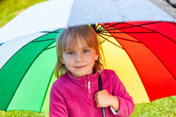 Little girl standing under umbrella in a rain outdoors