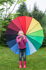 Little girl standing with umbrella in a rain catching raindrops outdoors