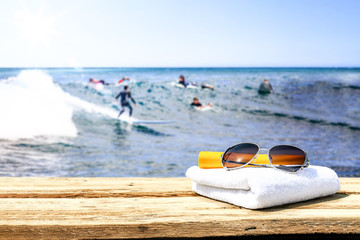 Wooden desk of free space for your decoration. Blurred background of surfers and waves . Blue ocean and white towel decoration. 