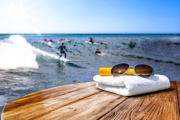 Wooden desk of free space for your decoration. Blurred background of surfers and waves . Blue ocean and white towel decoration. 