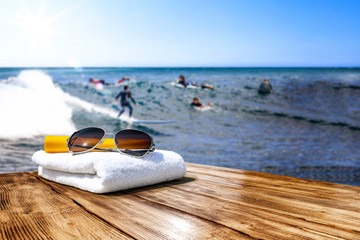 Wooden desk of free space for your decoration. Blurred background of surfers and waves . Blue ocean and white towel decoration. 