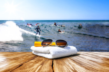 Wooden desk of free space for your decoration. Blurred background of surfers and waves . Blue ocean and white towel decoration. 