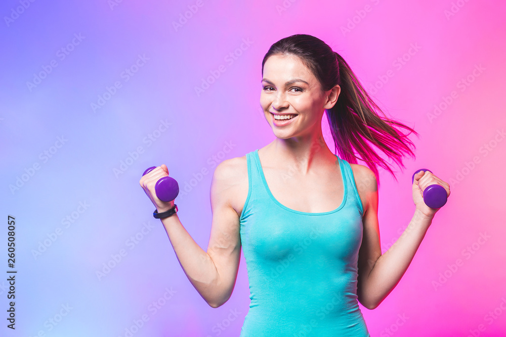 Wall mural portrait of young attractive happy woman in sport clothes with beautiful smile holding weight dumbbe