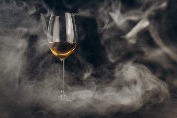 a glass of white wine on a black background. the smoke from the hookah envelops the glass. rest, holiday. alcoholic drink closeup. white fog