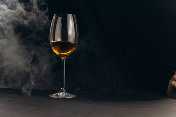 a glass of white wine on a black background. the smoke from the hookah envelops the glass. rest, holiday. alcoholic drink closeup. white fog