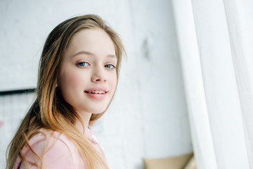 Joyful teenage kid in pink hoodie looking at camera with smile