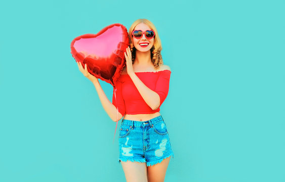 portrait happy smiling woman holding red heart shaped air balloon on colorful blue background