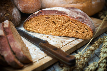 Sliced rye round bread and wheat ears with a knife on the old wooden table