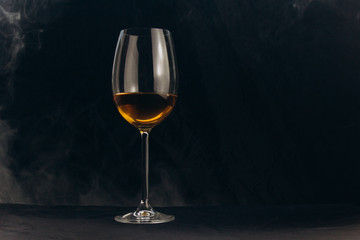 a glass of white wine on a black background. the smoke from the hookah envelops the glass. rest, holiday. alcoholic drink closeup. white fog